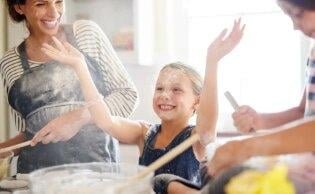 A small girl with her mom and hands in air is smiling in a deep cleaned kitchen with flour on their faces