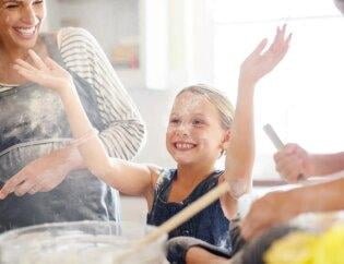 A small girl with her mom and hands in air is smiling in a deep cleaned kitchen with flour on their faces