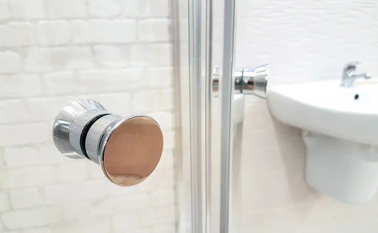 Shiny chrome door knob on a sparkling clean glass shower door after professional washroom deep cleaning by OnCleaning.