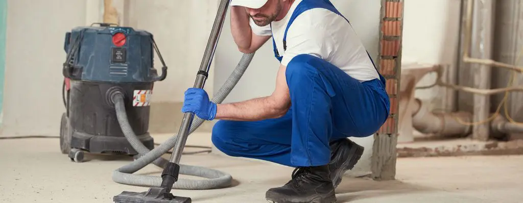 Post-Construction Cleaning Portsmouth - Industrial Vacuum Services Professional cleaner in blue uniform using industrial wet-dry vacuum to remove construction dust and debris from unfinished building site