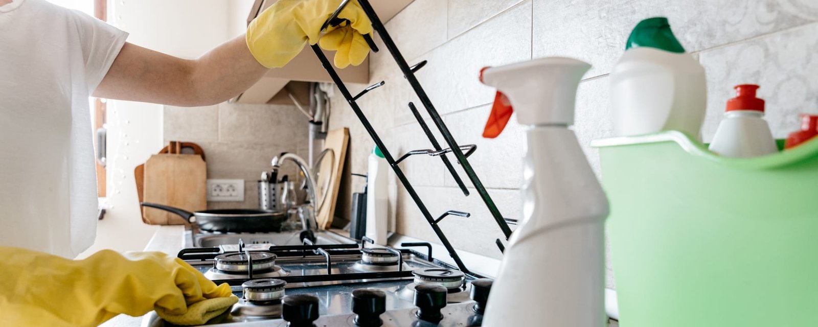 Detail Cleaning Stove in a Southampton Home Kitchen A person wearing yellow gloves cleaning a gas stove top in a Southampton home kitchen using spray cleaner and microfiber cloth.