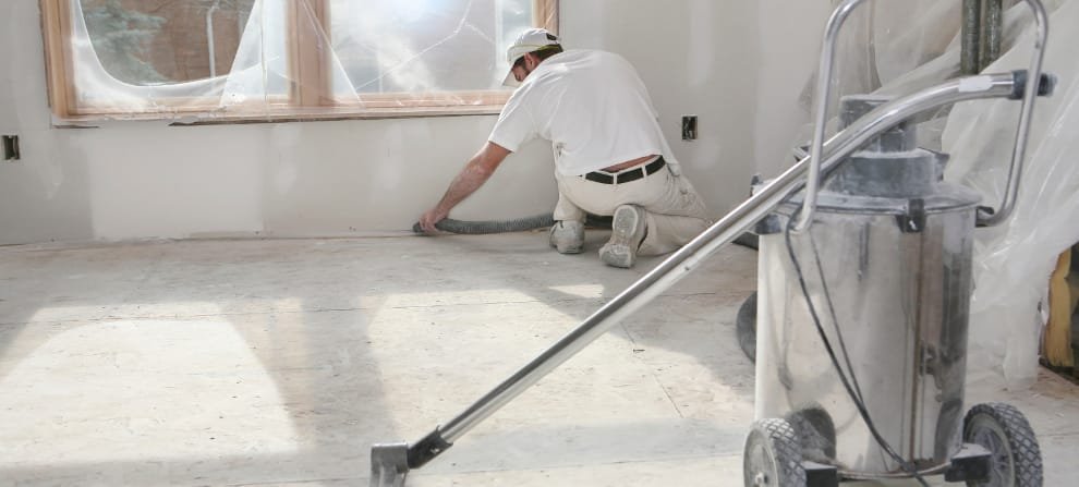 Professional Construction Cleanup Services Portsmouth - Dust Removal Construction worker in white protective clothing operating commercial vacuum cleaner on concrete floor during post-construction cleanup phase