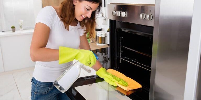 Oven Cleaning A female cleaning using a steam cleaning machine to clean an oven interior.
