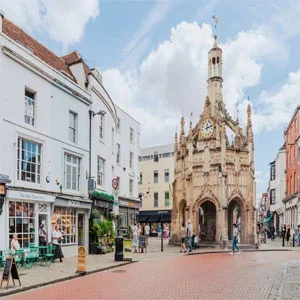 A picturesque view of the historic Chichester Market Cross, a striking medieval monument rising above the charming shops and architecture of Chichester's quaint city center.