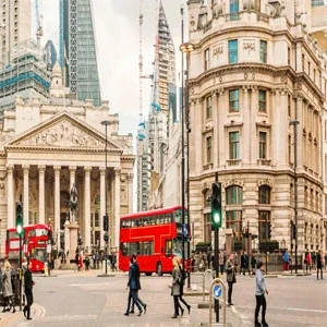 Bustling street scene in central London, with iconic red double-decker buses, pedestrians, and historic architecture in the background.