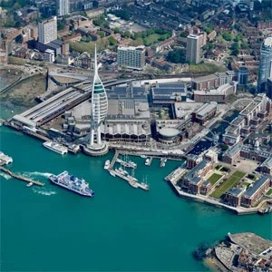 Aerial view of the historic Portsmouth Harbor, featuring the iconic Spinnaker Tower, residential and commercial buildings, and numerous boats and ships docked along the waterfront